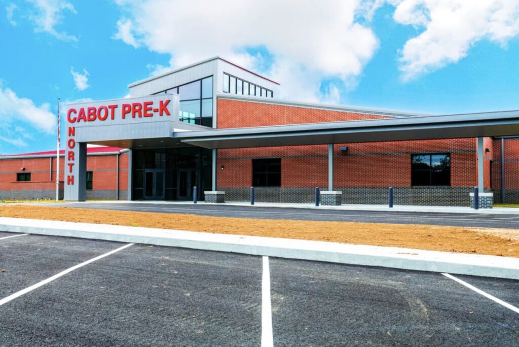 A modern brick building with large windows and a covered entrance labeled CABOT PRE-K NORTH, seen from an empty parking lot under a partly cloudy sky.